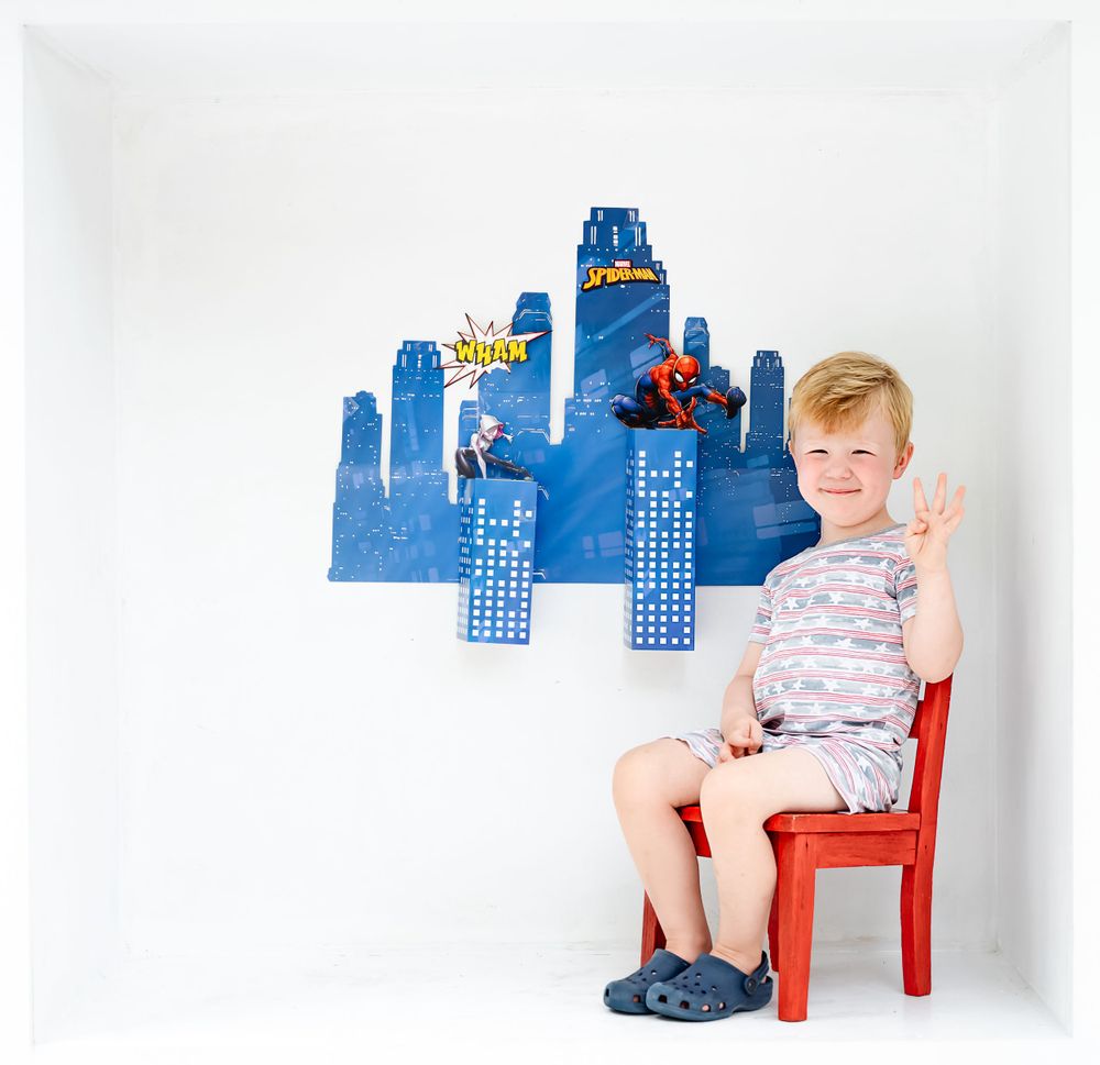 Blue city skyline backdrop with small red chair for birthday photoshoot setup.