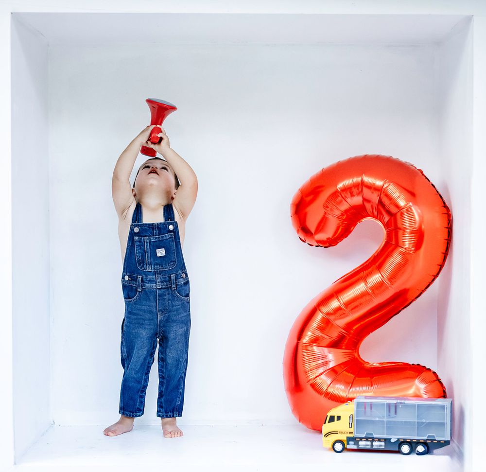 Construction-themed birthday photo with red number 2 balloon and toy train.