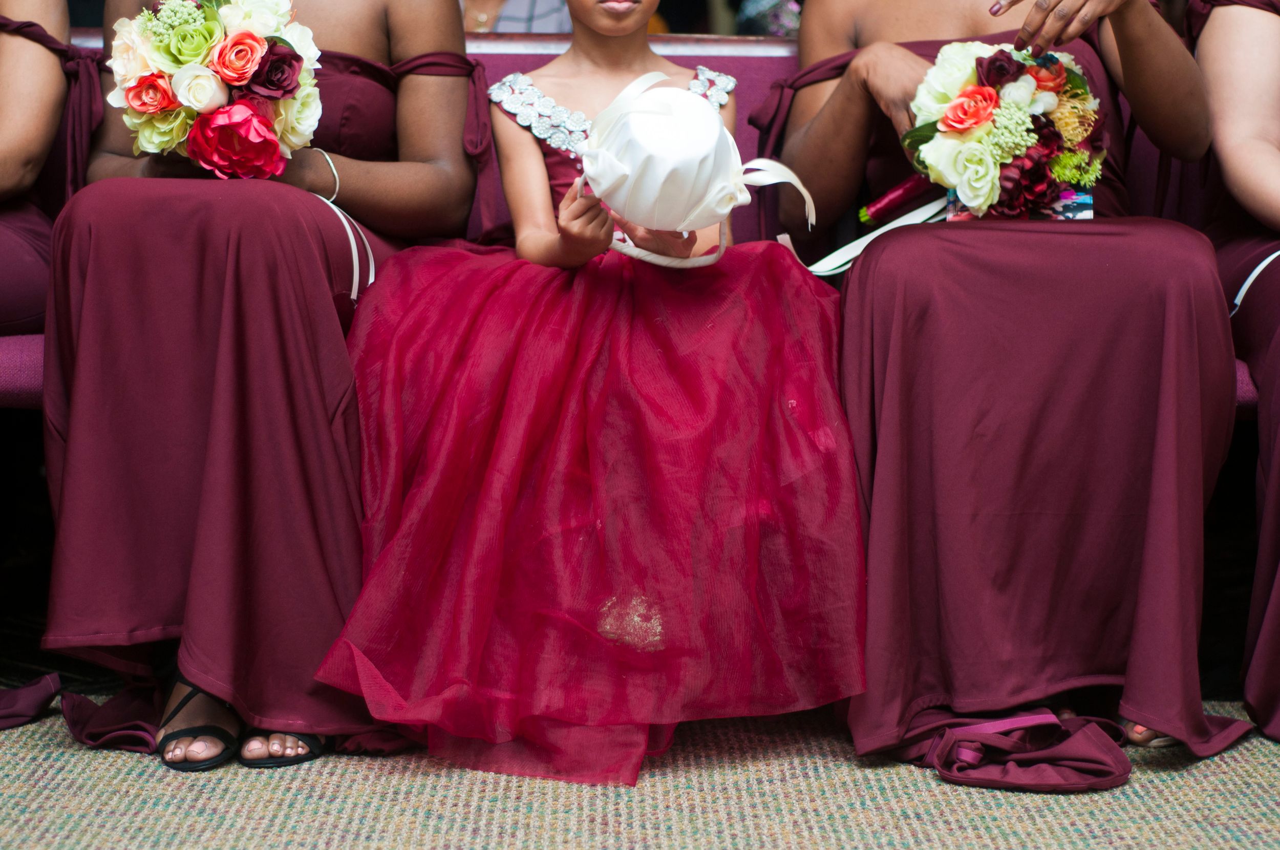 The flower girl sits in the middle of the bridesmaids, holding her flower basket while the bridesmaids hold their bouquets.