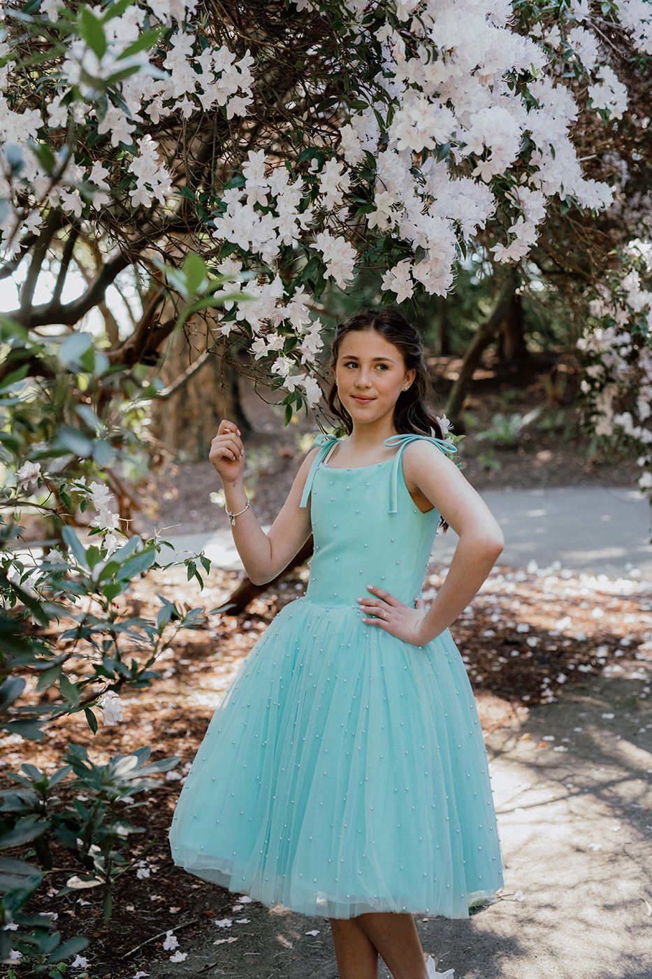 A girl in a light blue dress with pearl accents stands among blooming white flowers in a serene garden setting. Dublin botanic garden.