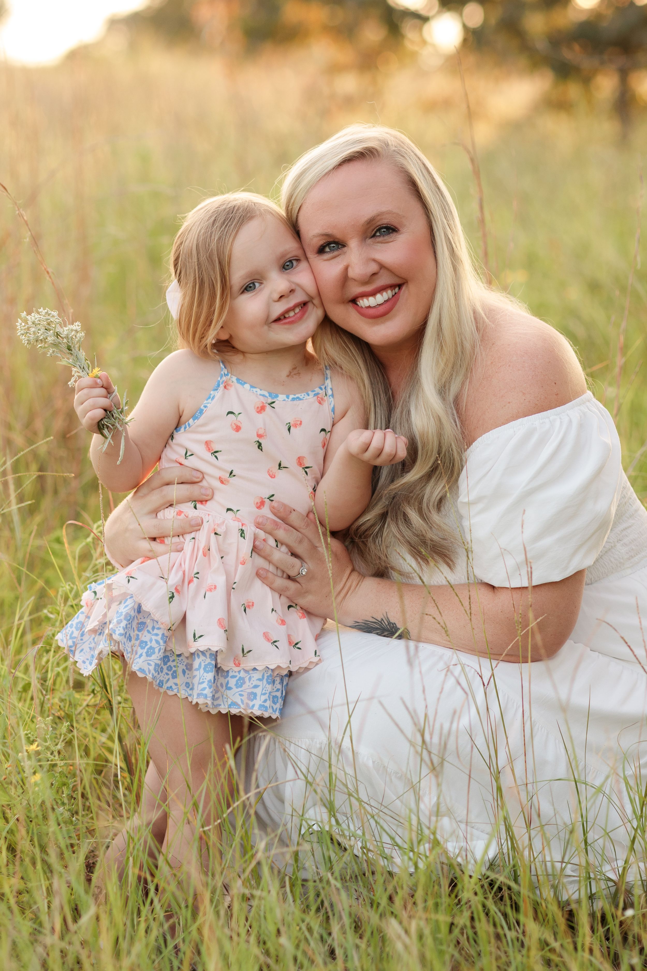 Mother and daughter share tender moments together in a sunlit meadow with wildflowers during golden hour.