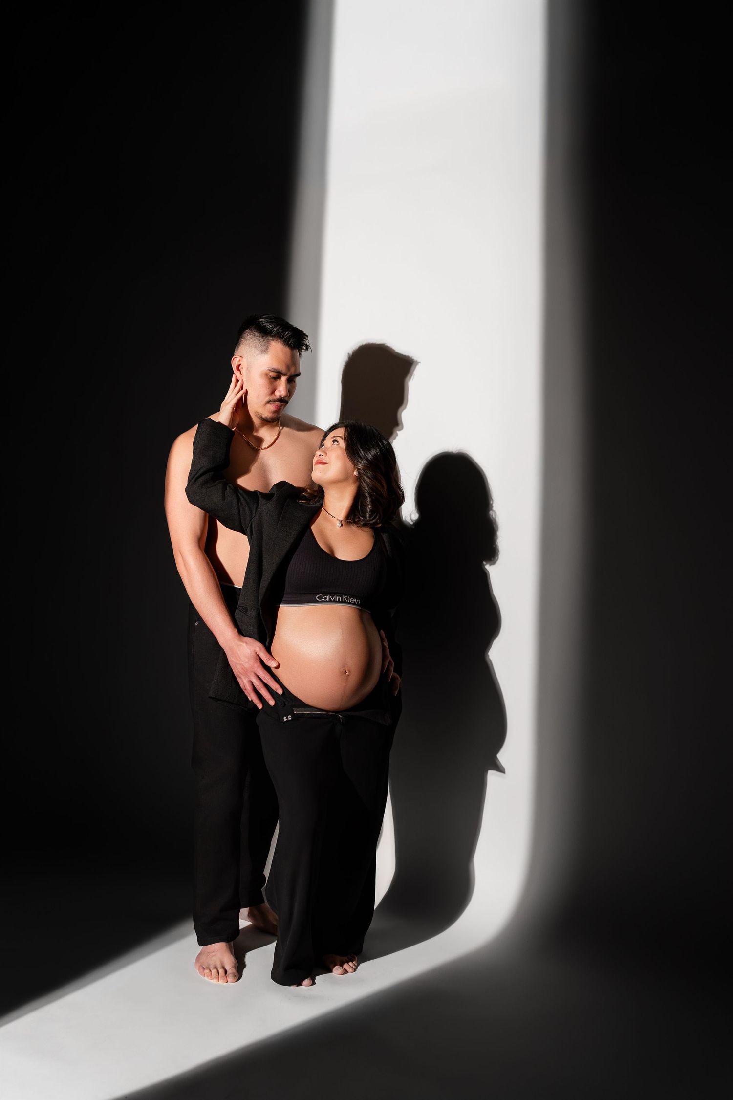 Artistic black and white maternity photos with dramatic lighting and shadows against a white backdrop.