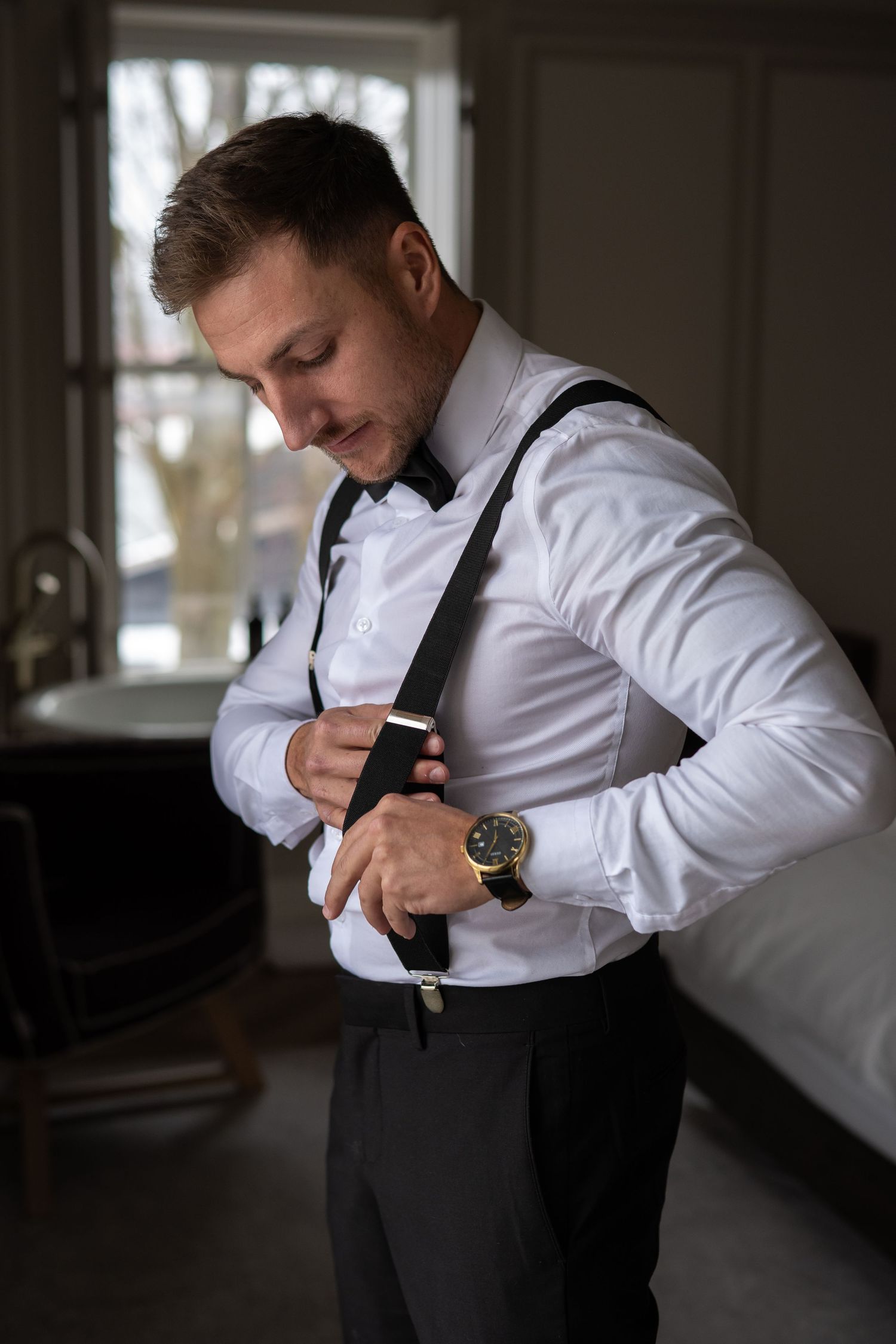A person in a white dress shirt adjusts their tie while getting dressed in a dimly lit room. Royal Hotel Picton
