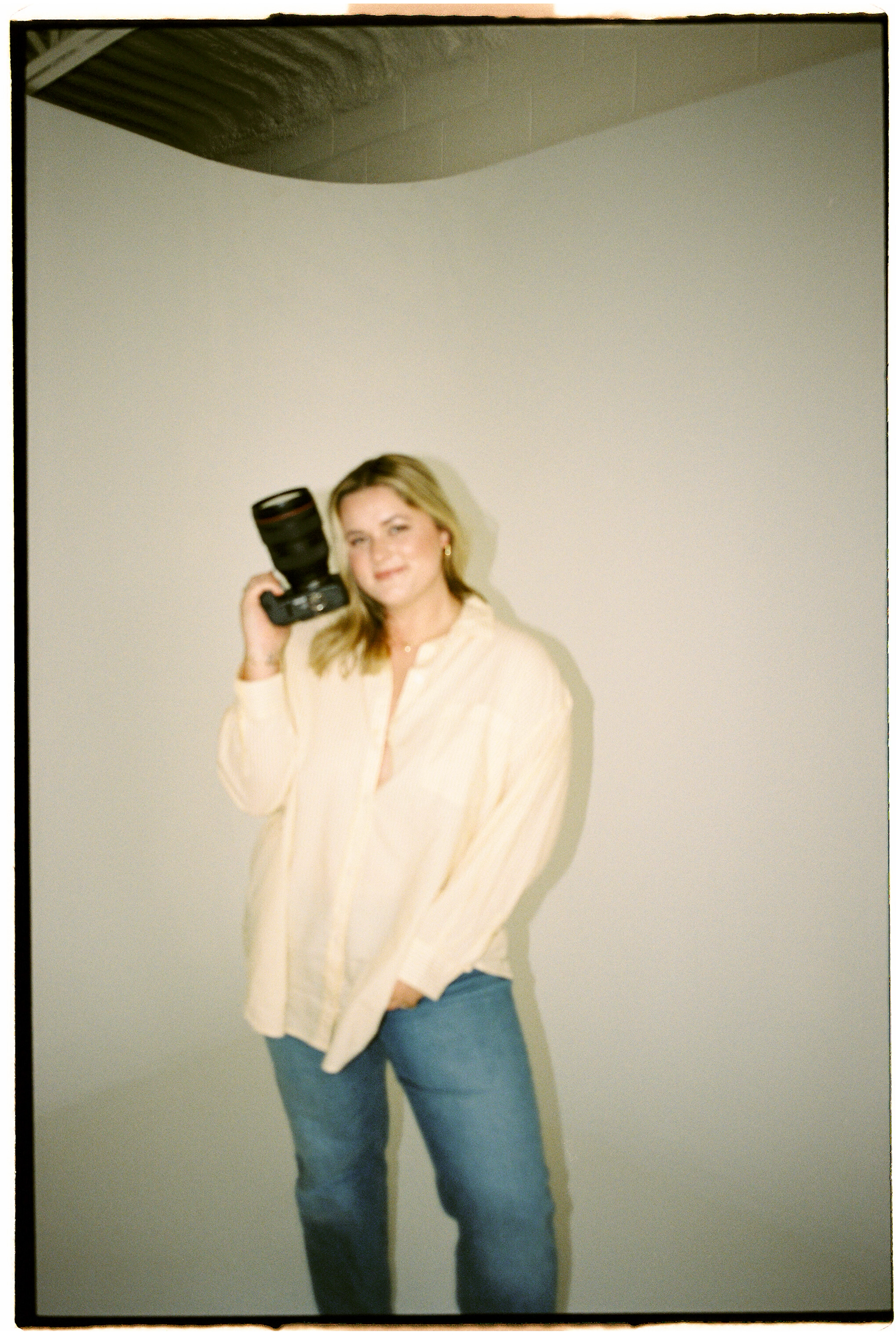 Woman in casual white tank top and light denim poses against beige background.