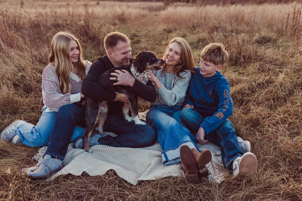 A group sits together on a blanket in a golden autumn field during sunset.