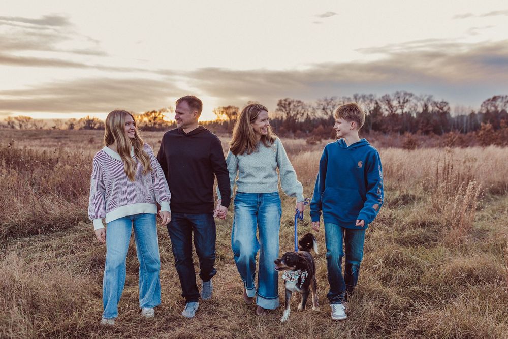 A group of people in casual clothing walking together through a golden field at sunset.