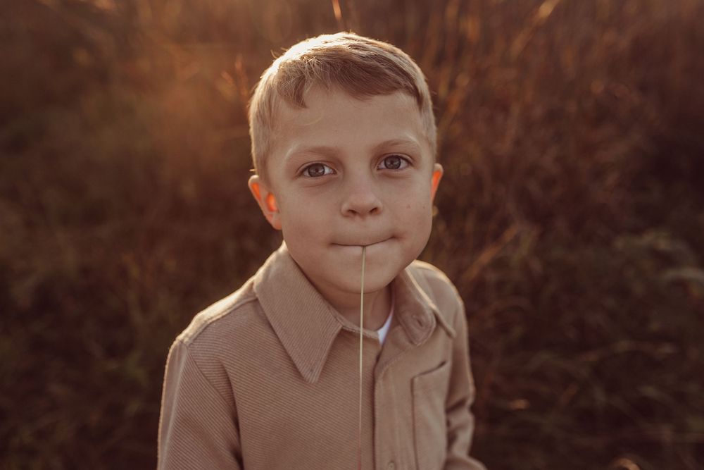 A young boy in a beige collared shirt poses outdoors during golden hour with warm lighting and a blurred background.