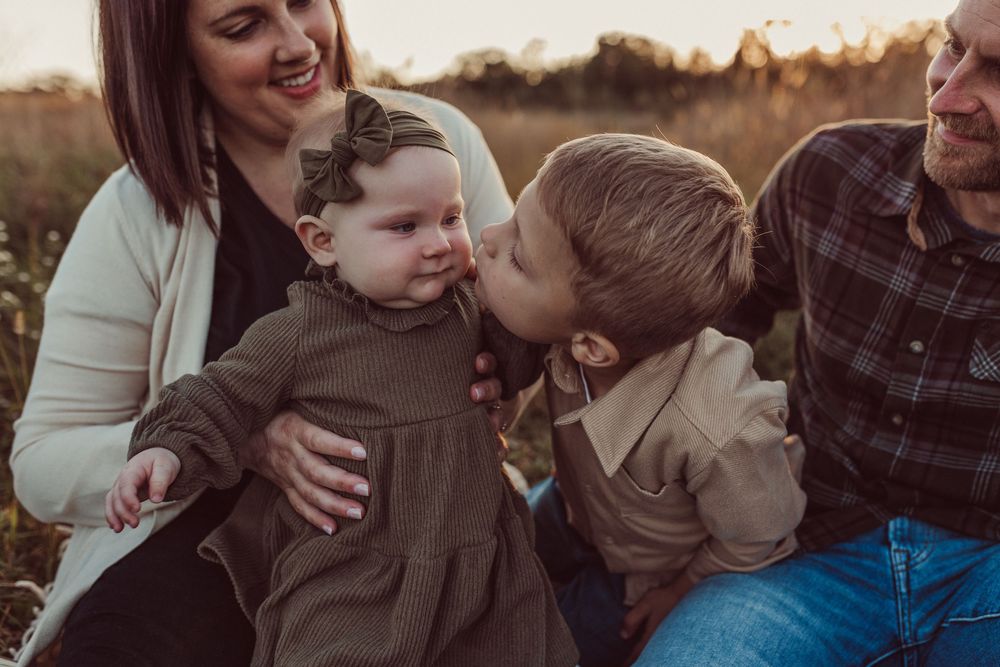A candid family photo session in a golden field at sunset shows joyful moments and natural interactions.