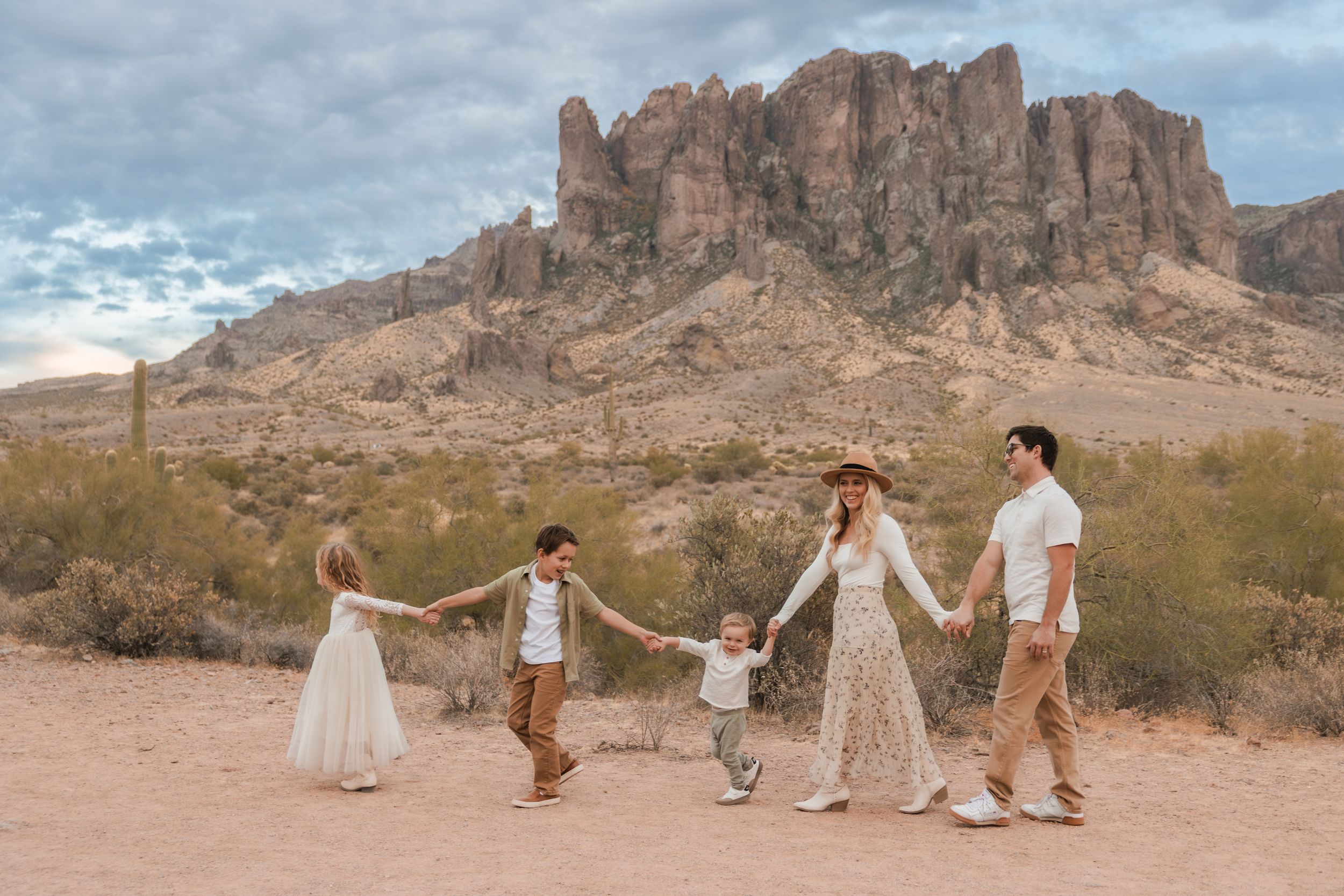 A group walks hand-in-hand through the rugged desert landscape of Superstition Mountains in Arizona at sunset.