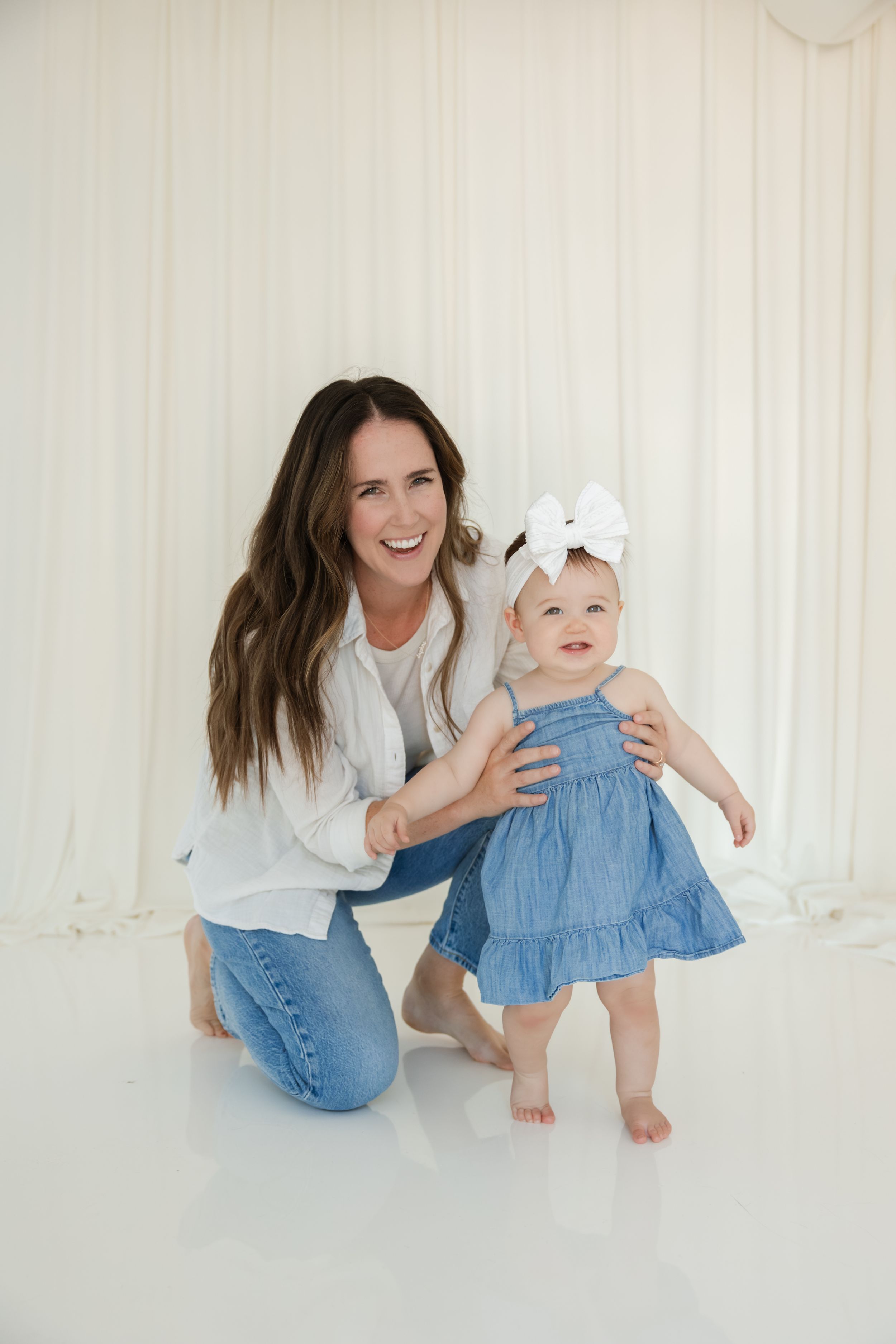 A joyful moment captured in a bright white studio as parent and baby in denim and blue dress play together.