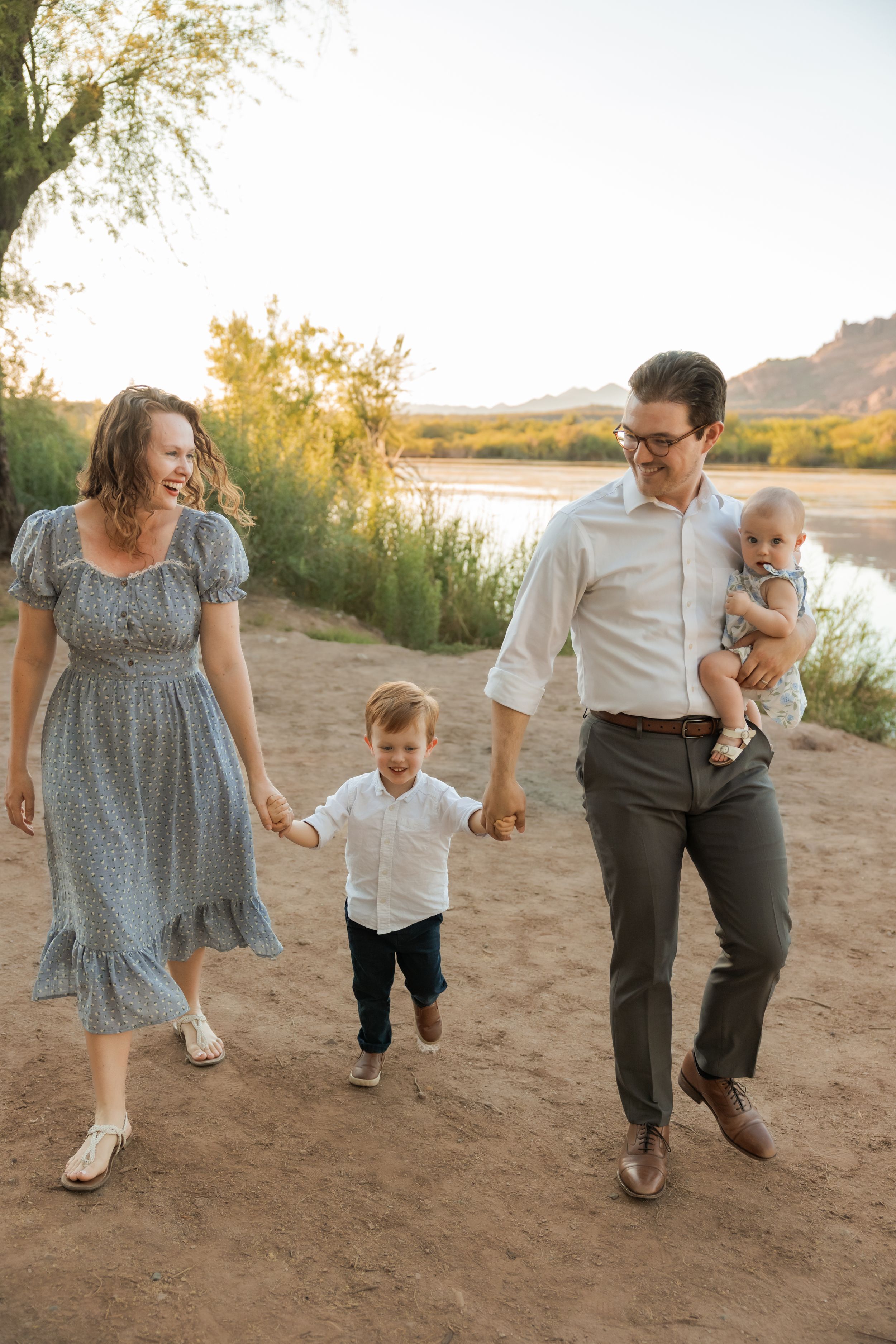 Family walking and playing together on sandy path beside lake during golden sunset hour.