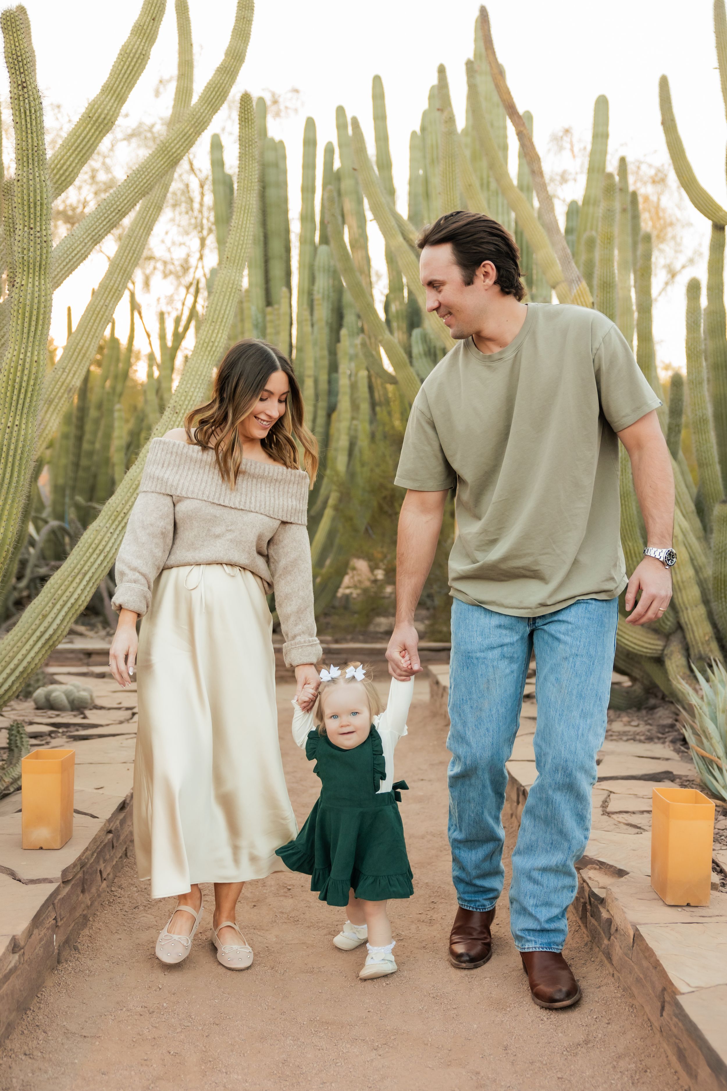 Three image sequence shows people walking together through a desert cactus garden with rustic lanterns at sunset.