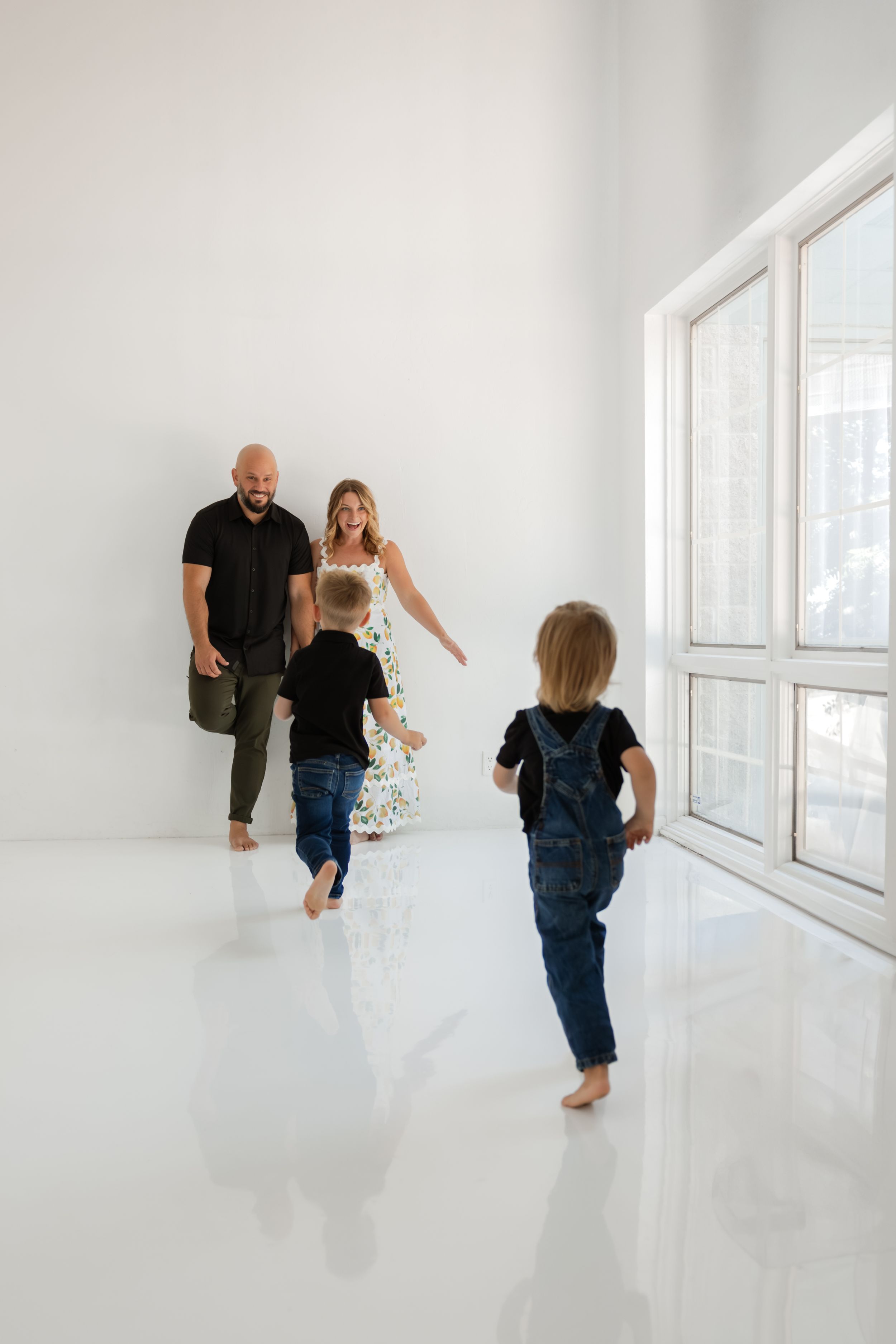 A sequence of playful moments unfolds in a bright white room as a child runs towards adults in a candid family scene.