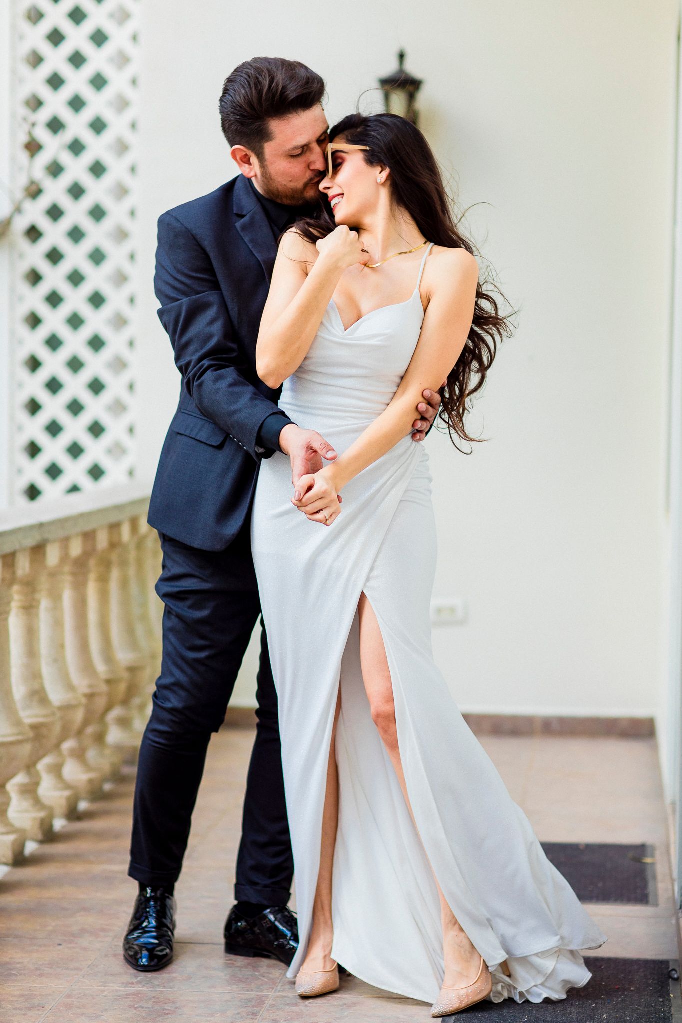 Elegant couple in formal wear sharing an intimate moment on a balcony.