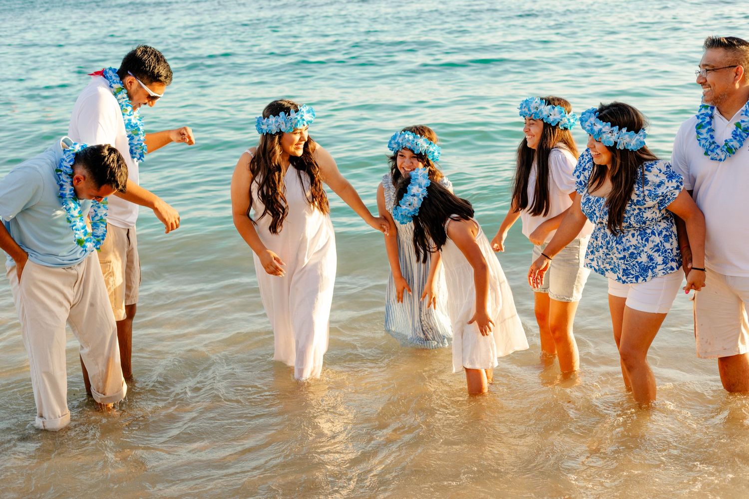Wedding party plays in the ocean waves wearing coordinated blue and white outfits.