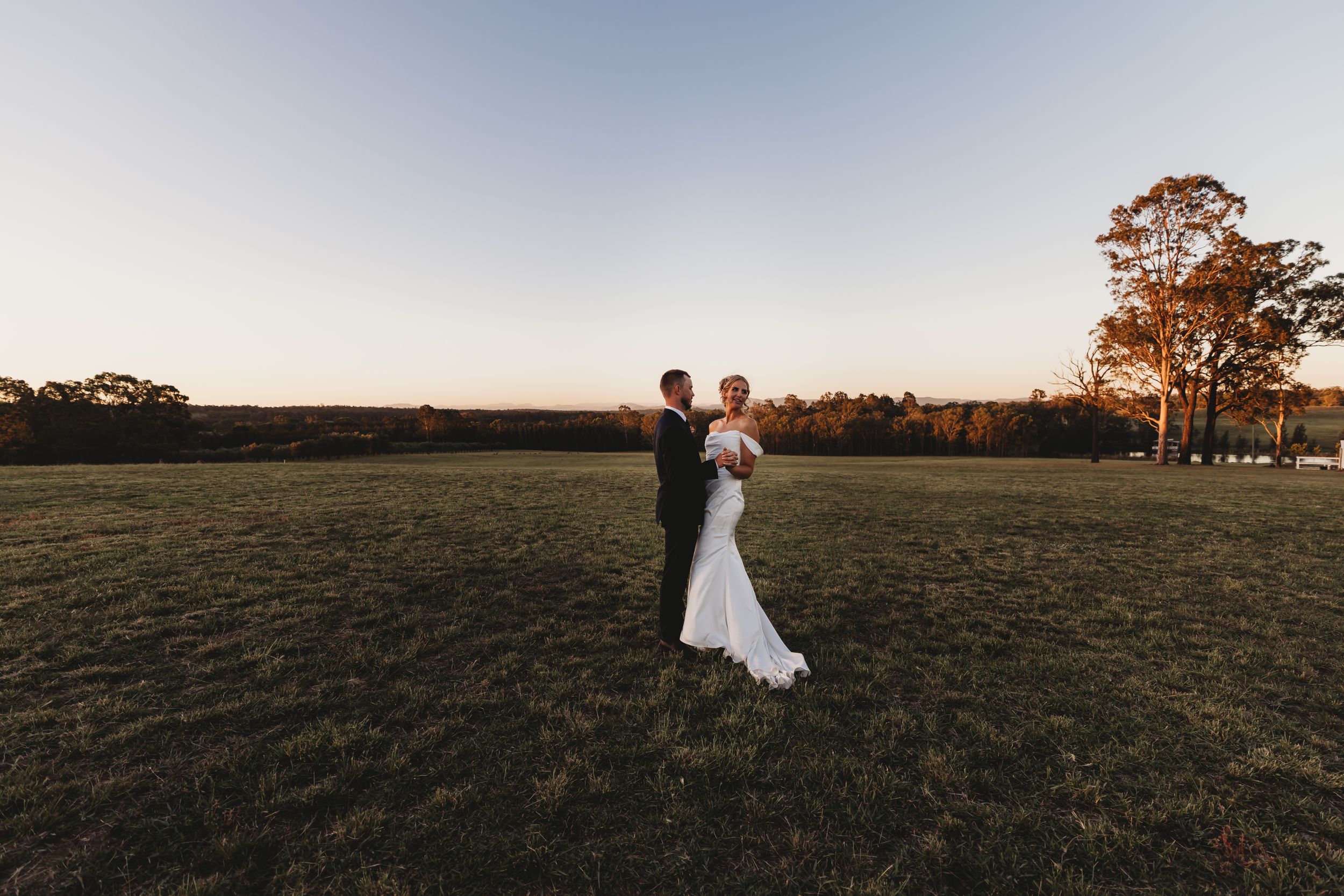 Bride and groom share a romantic moment in an open field at golden hour during their outdoor fall wedding.