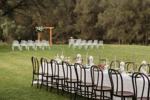 Wedding reception setup with elegant wooden chairs and tables arranged outdoors on green lawn.