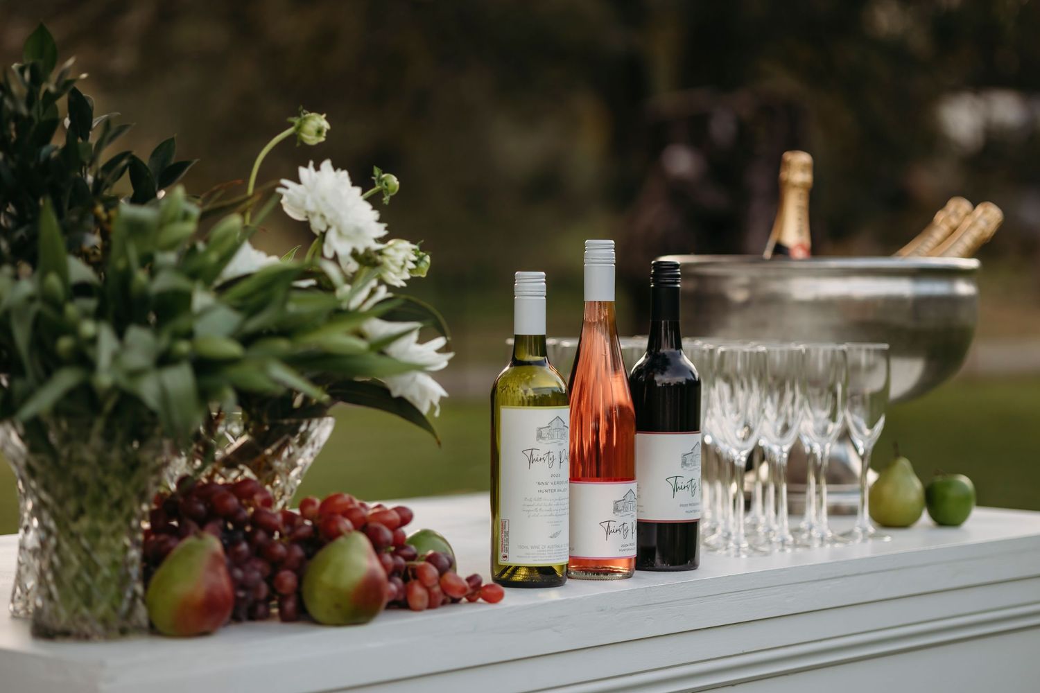 Wedding reception table decorated with fresh fruit, wine bottles, and elegant glassware.