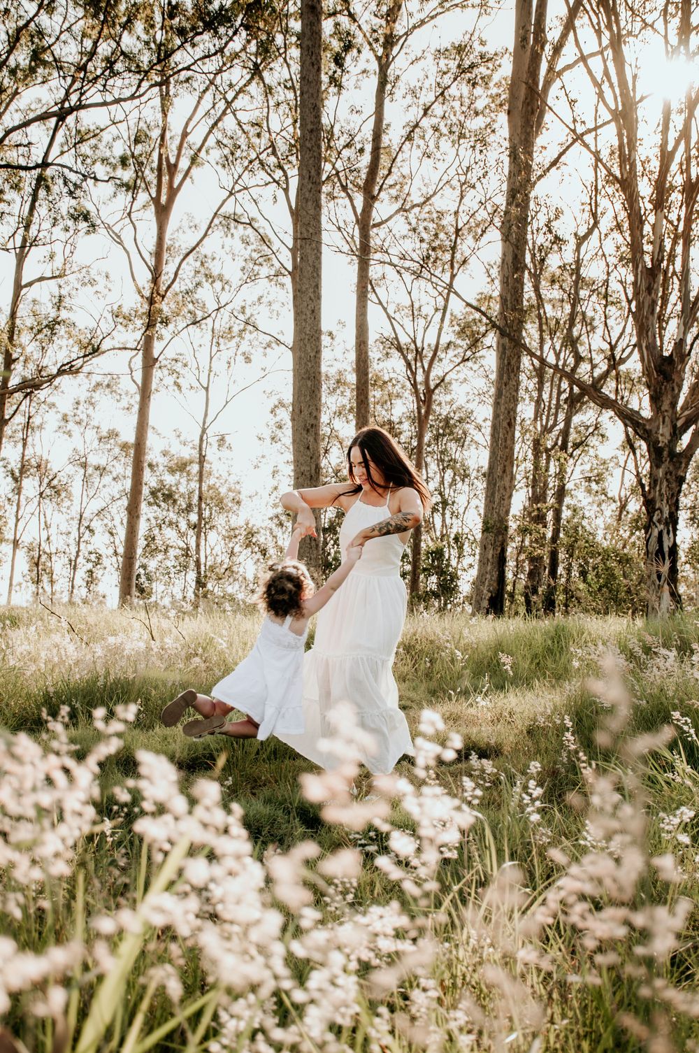 mum and daughter playing in the grassy field at sunset. mum spinning daughter around during a family photoshoot