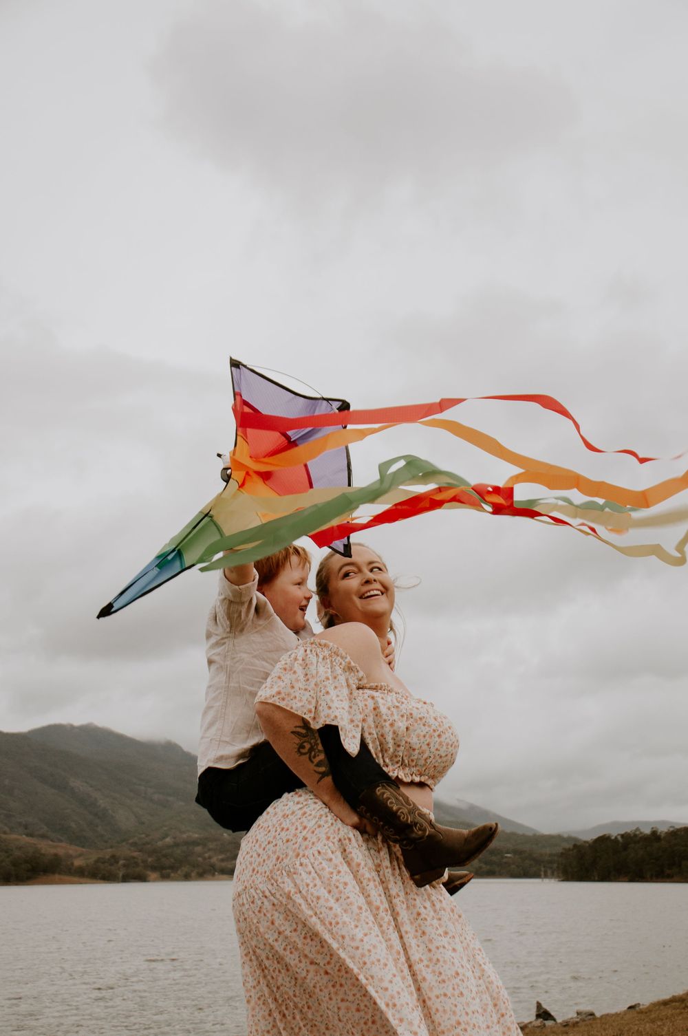 mum and son playing with the kite during a windy day on the lake with mountain views