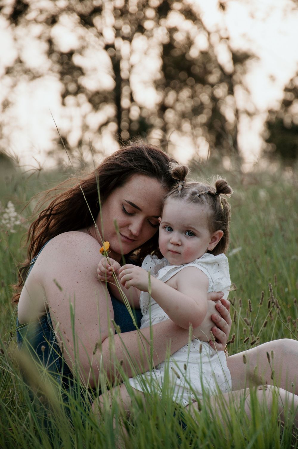 mum and bub cuddling in the long grassy field. mum and daughter photoshoot with flowers