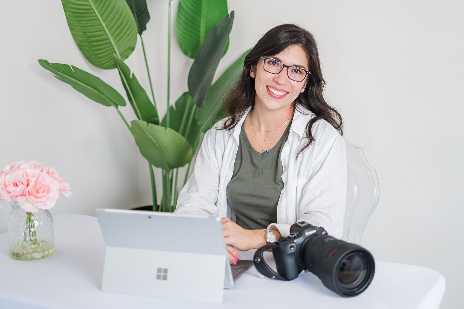 Professional photography workspace with plants, laptop and camera equipment on white desk.