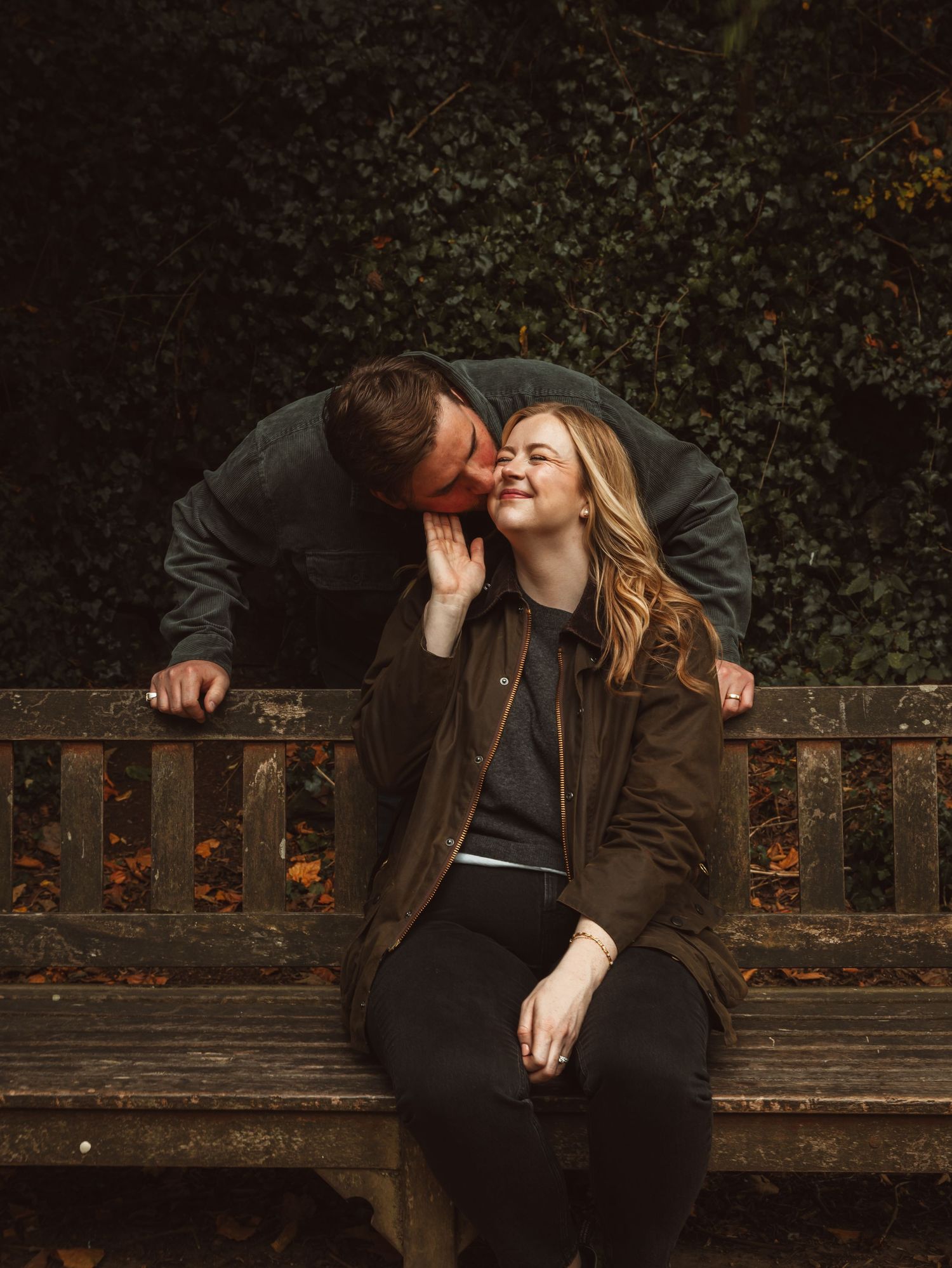 Couple sharing tender moments on rustic wooden bench in evening light.