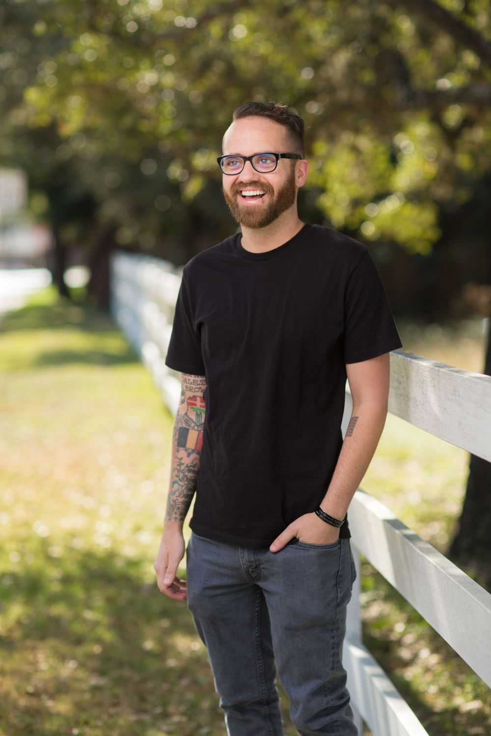 Casual portraits against white fence wearing black t-shirt and jeans.