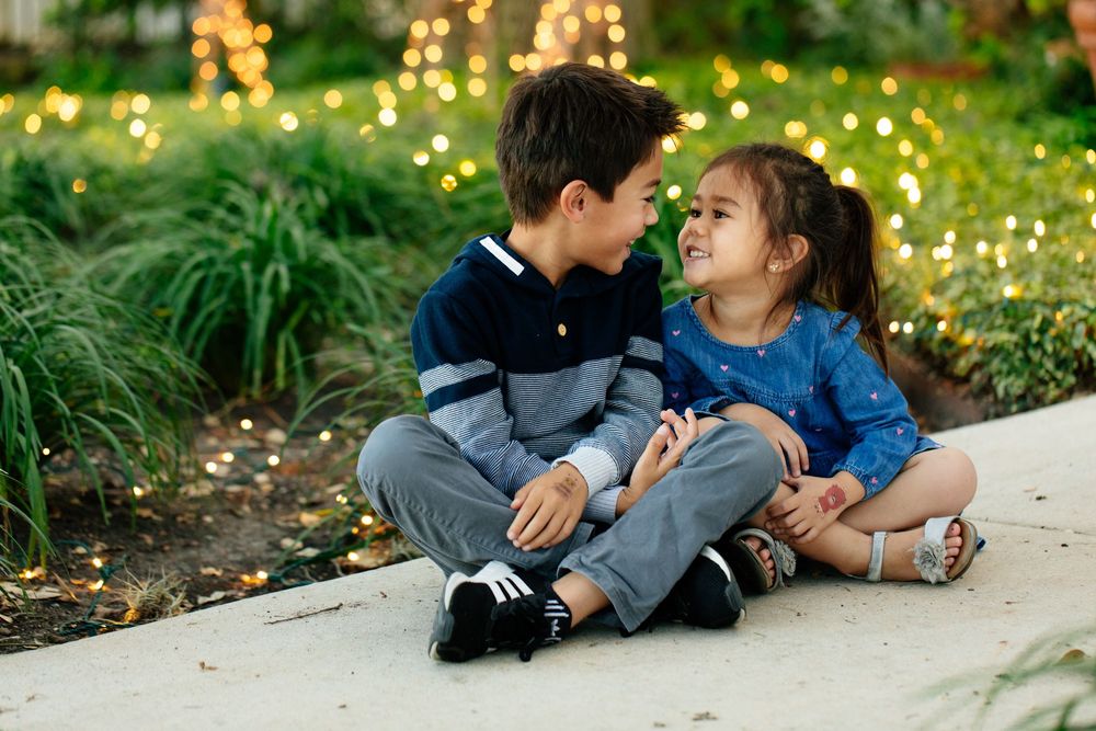 Intimate family portrait session on ground with twinkling bokeh lights and natural greenery in background.
