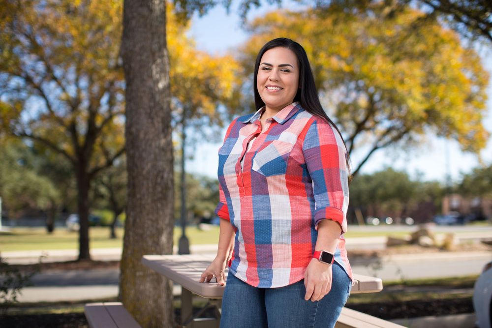 Outdoor portrait with red plaid shirt against autumn trees and wooden fence.