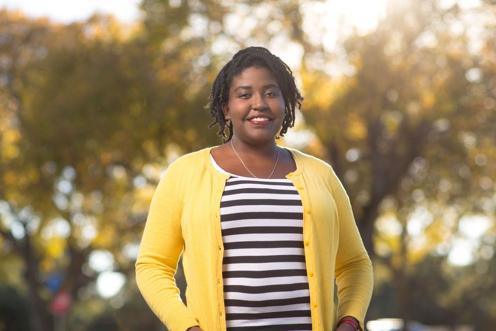 Person wearing yellow cardigan and striped shirt smiling outdoors during autumn season.