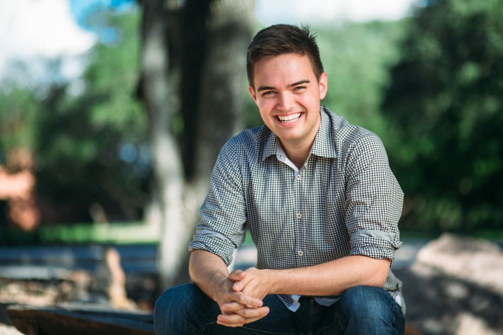 Casual outdoor portrait of someone in grey checkered shirt sitting outdoors.