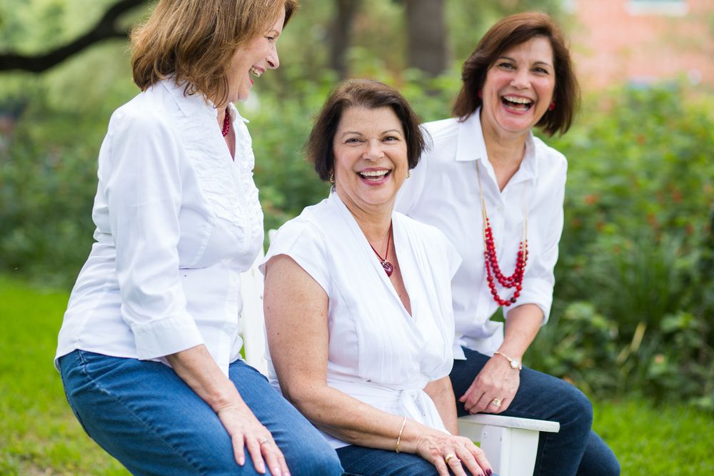 Three people sit outdoors laughing together while relaxing on a garden bench in summer.