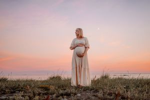 Gravid kvinna vid havet under rosa himmel