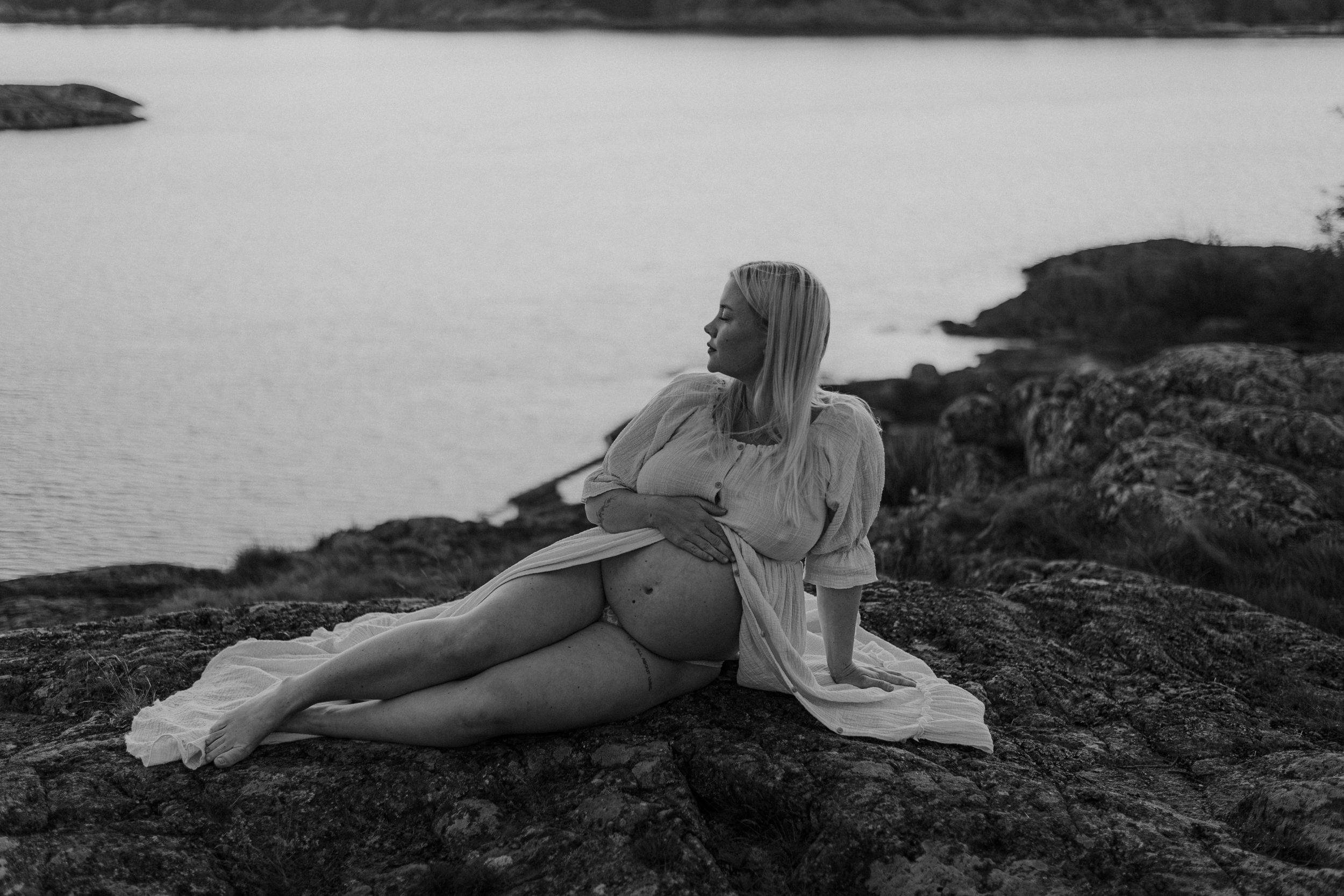 Svartvit bild kvinna sitter på klippa med bar mage