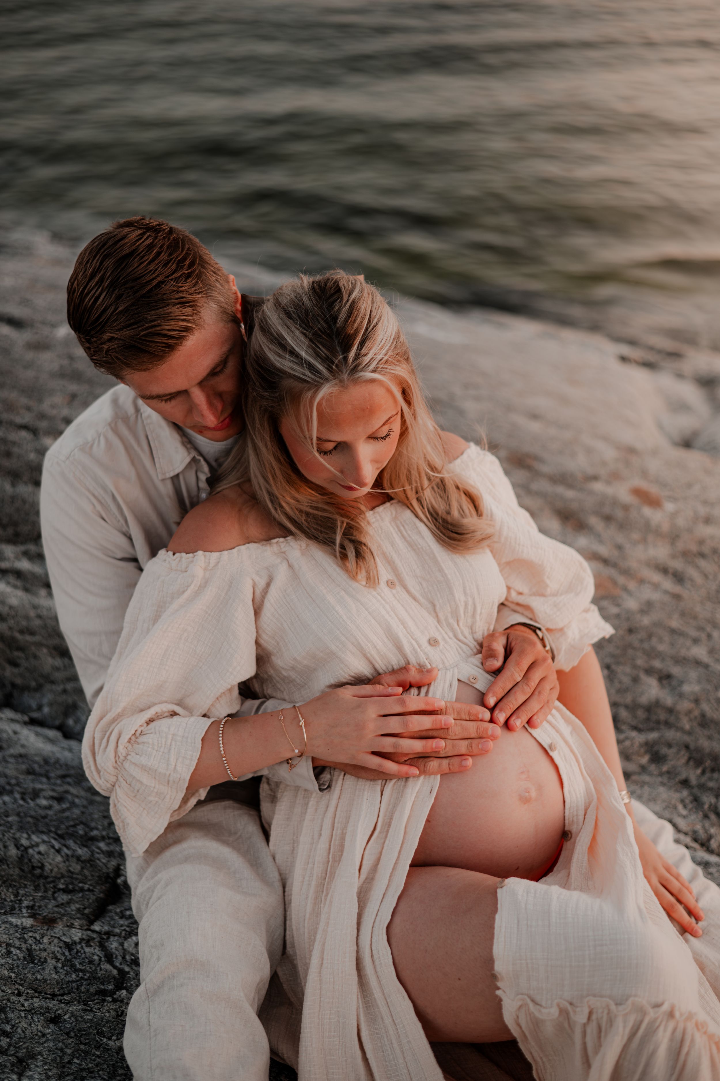 Gravidpar sitter på ett berg och håller händerna på magen