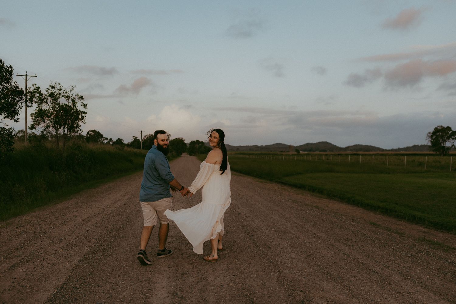 Couple playfully dancing on a rural dirt road at dusk during a maternity photoshoot.