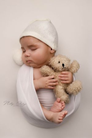 Slapende newborn in witte wrap met beertje tijdens newbornshoot in Goes