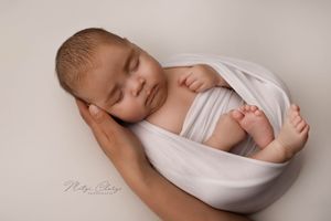 Slapende newborn in witte wrap met hand van mama tijdens newbornshoot