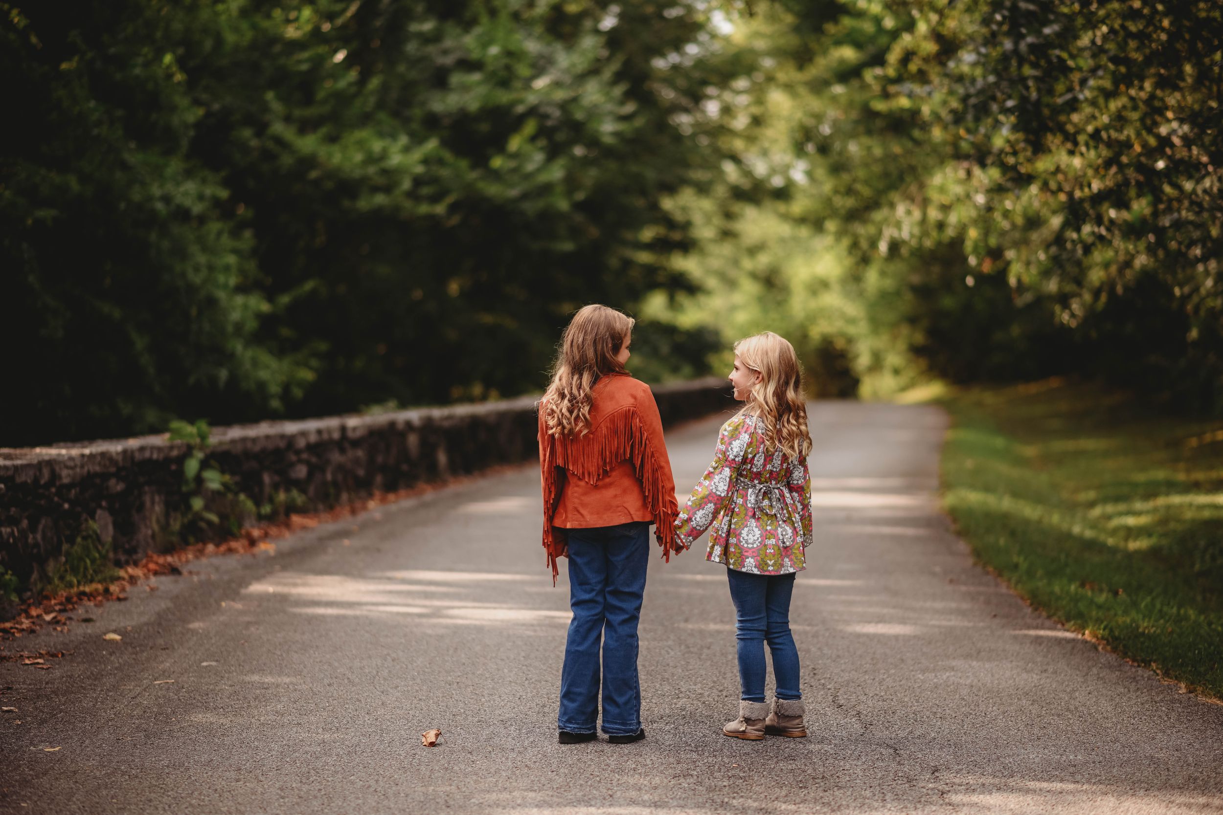 Two children walking hand in hand down a tree-lined path.