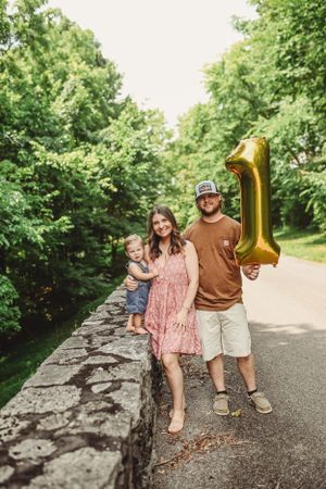 A family photo on a stone wall path with someone holding a gold number one balloon.
