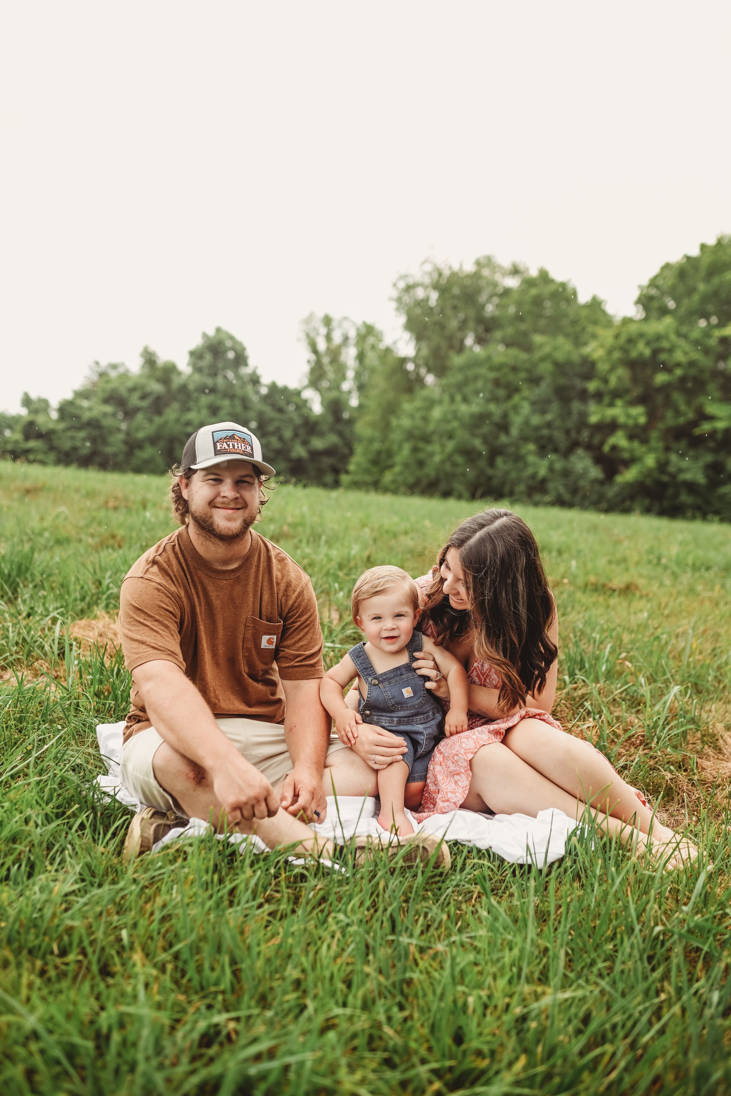 Family relaxes together on a grassy field during a summer afternoon photo session.