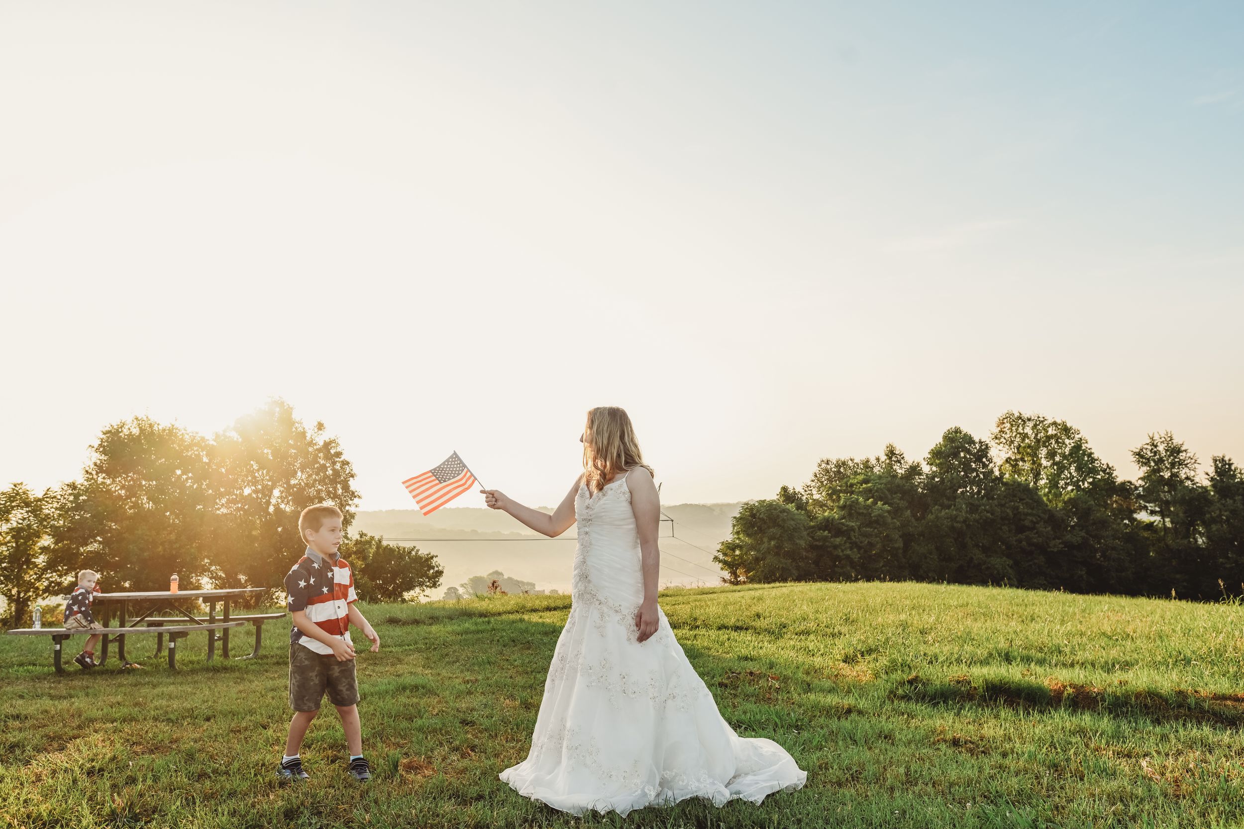 Wedding couple dances in an open field at sunset with golden light streaming behind them.
