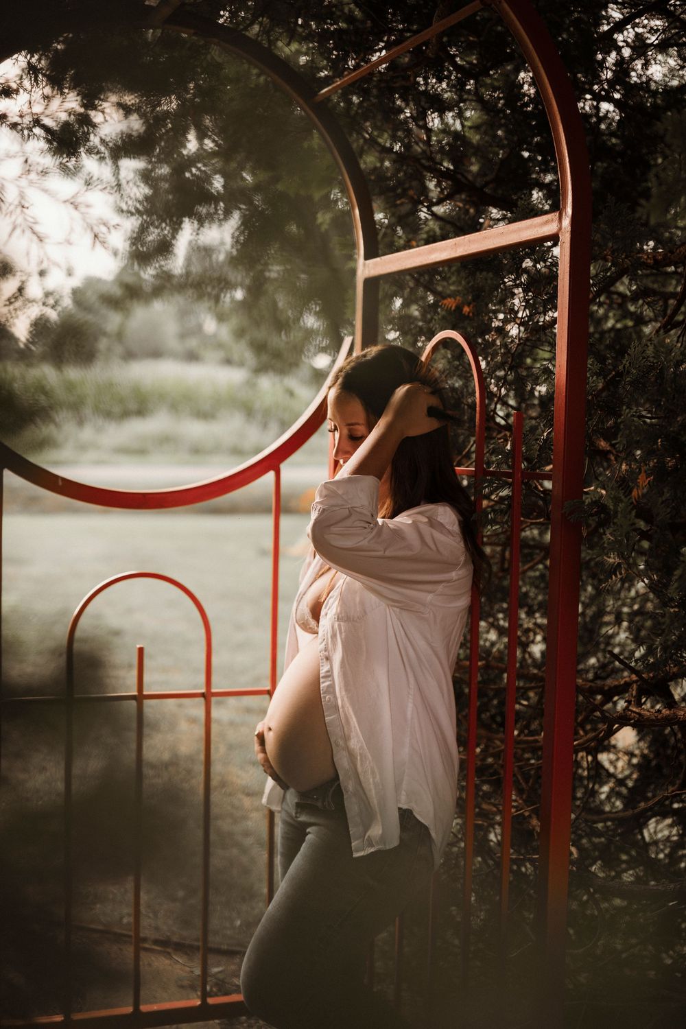 A person in a flowing white dress leans against red metal railings in a misty forest setting at dusk.