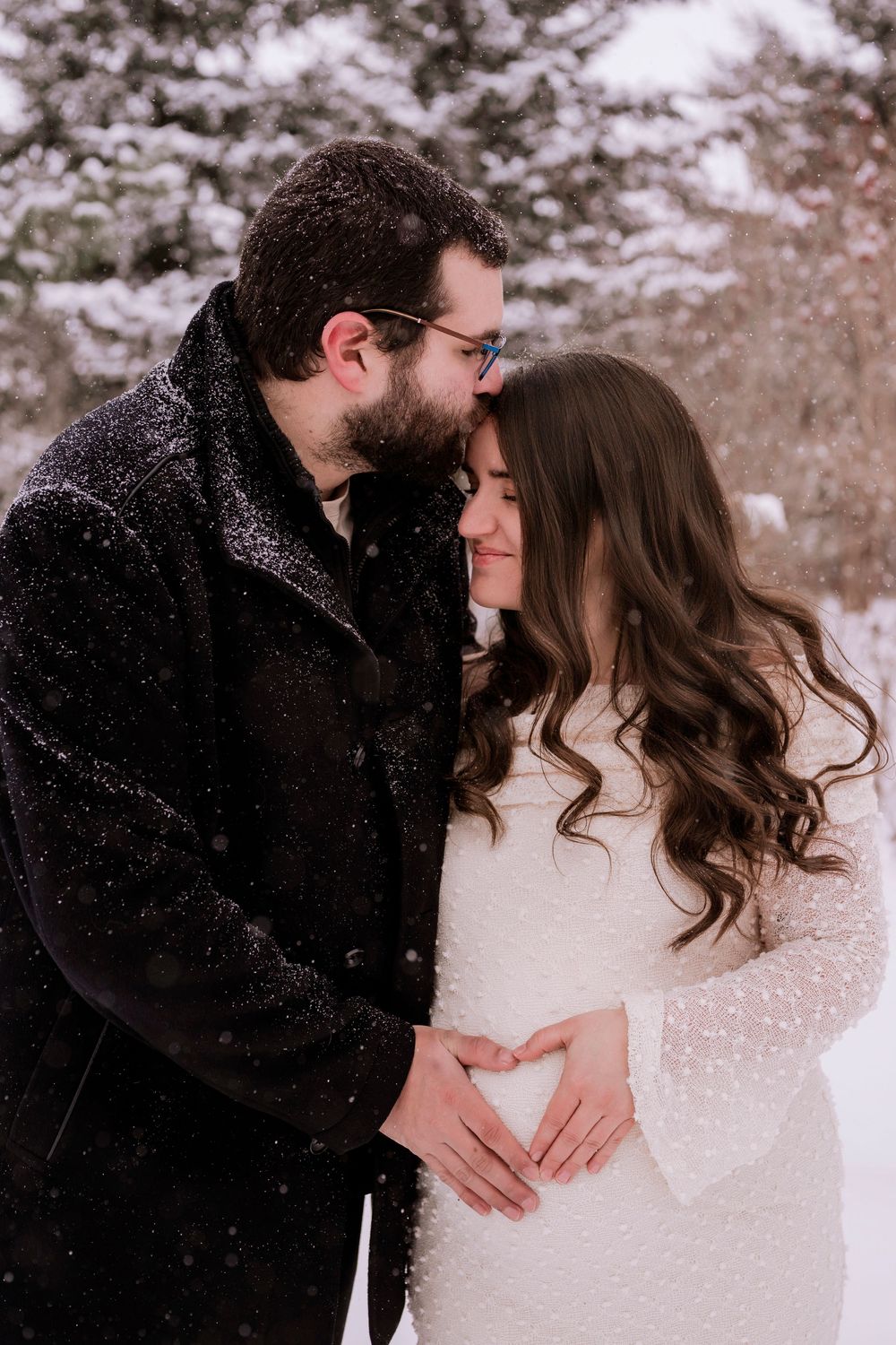 A romantic couple shares intimate winter moments in the snow, with the woman wearing a white dress and man in black coat.