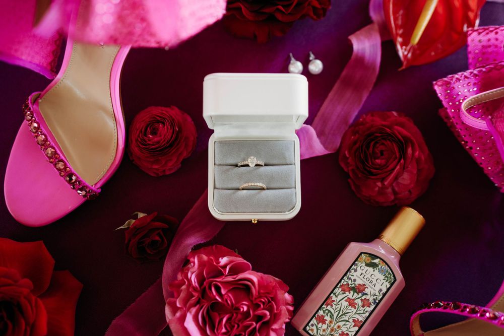 Diamond engagement ring in white box surrounded by red roses and pink wedding accessories.