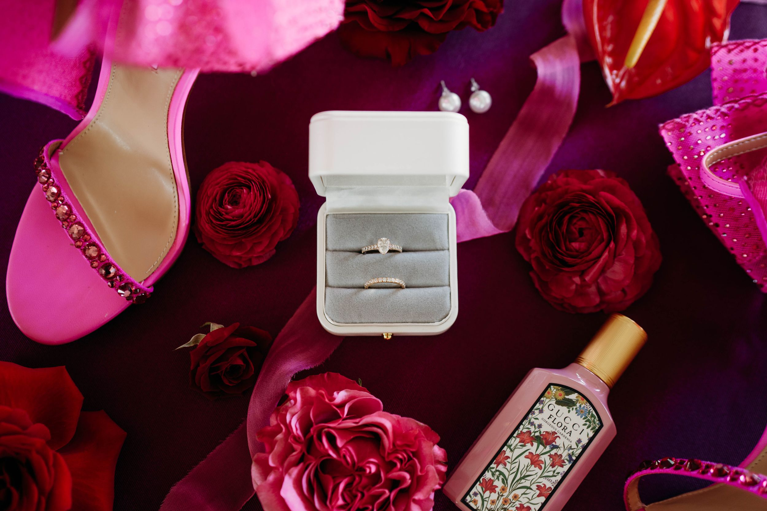 Diamond engagement ring in white box surrounded by red roses and pink wedding accessories.