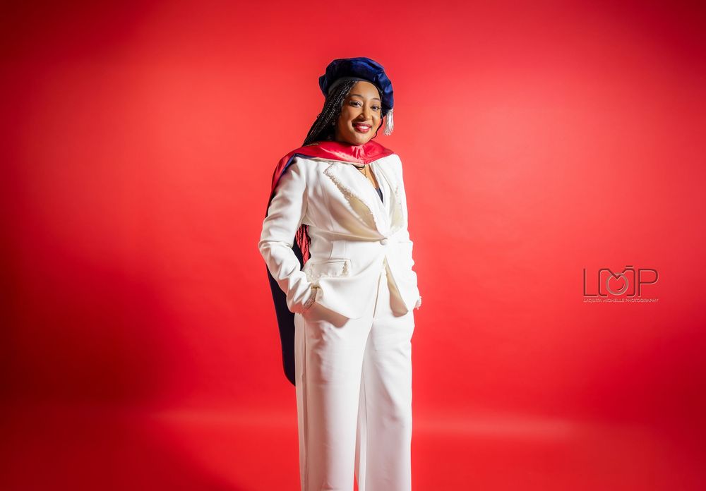 A person in an elegant white pantsuit stands confidently against a vibrant red background in a studio setting.
