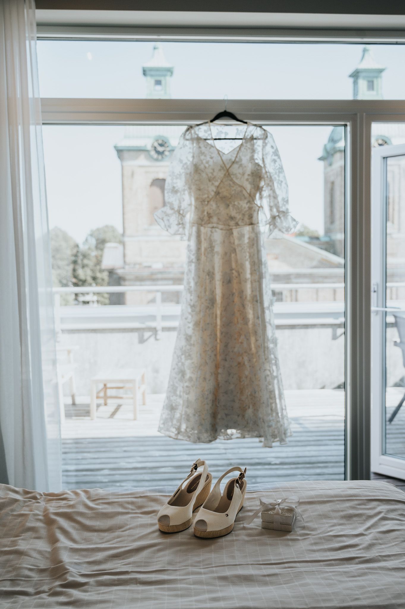 A series of wedding detail photos showing a lace dress hanging in a window and elegant white heels on a bed.
