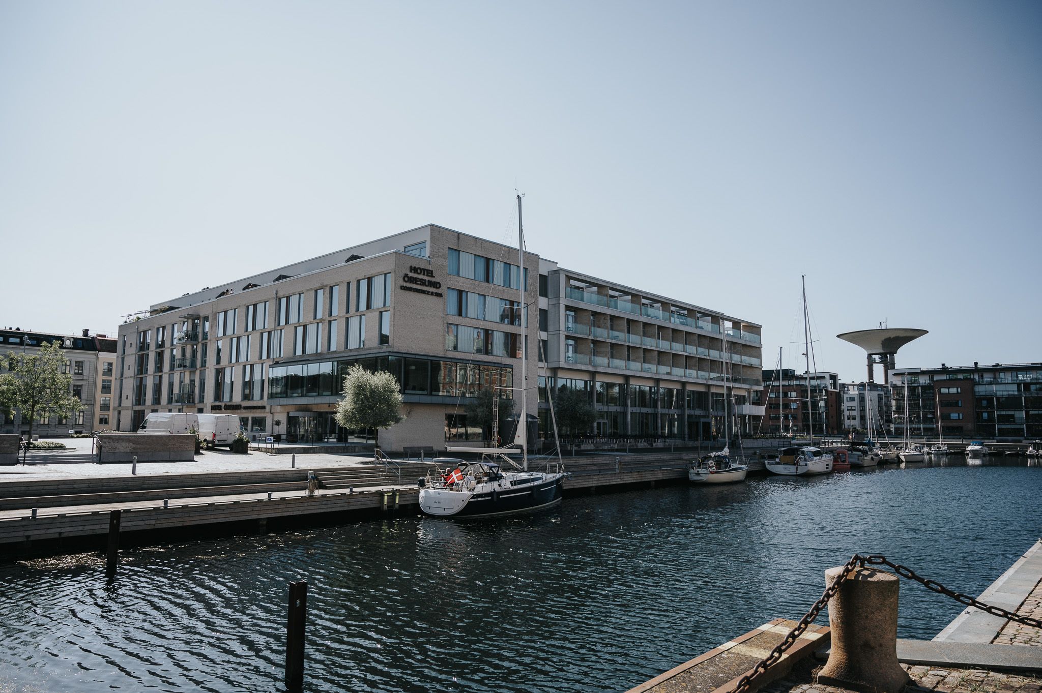 Modern waterfront building complex with boats docked along a marina in an urban harbor setting.